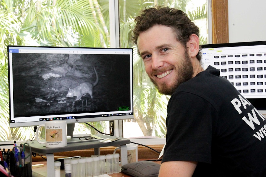 An image of a man looking at a quoll pictured on a computer screen.