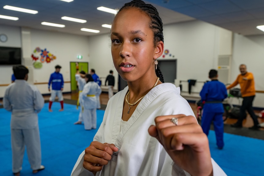 A girl wearing a taekwondo uniform shows her fists to the camera