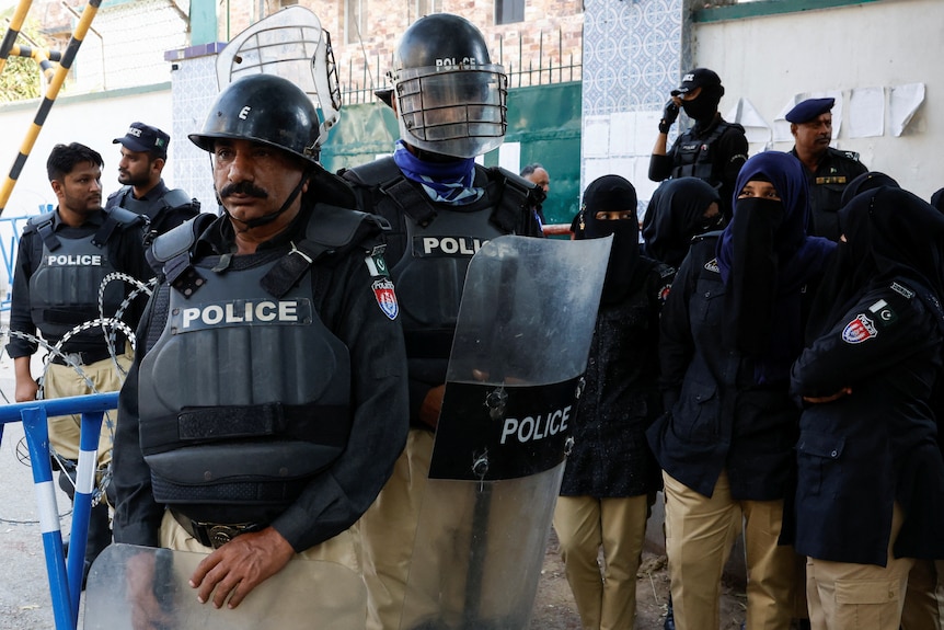 Pakistan police wearing shields and body armour stand guard near a protest in Karachi