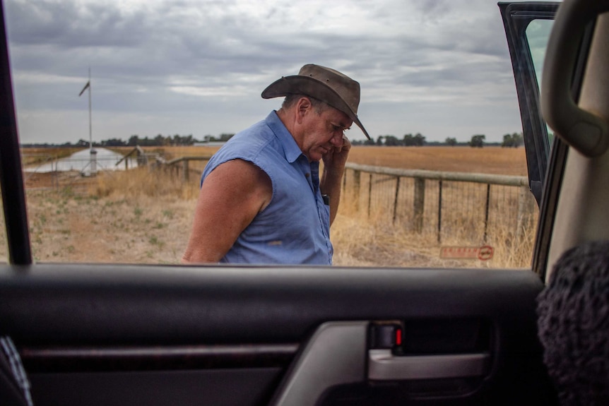 A farmer speaks on his phone, standing beside a ute.