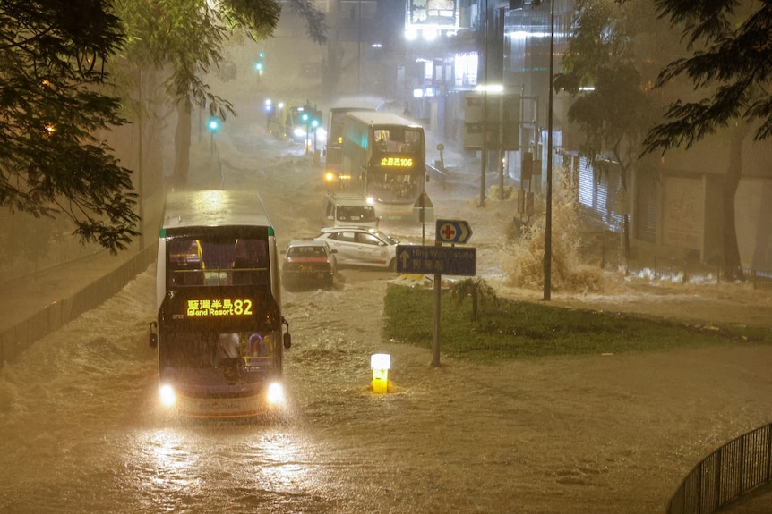 A bus drives through a flooded street.