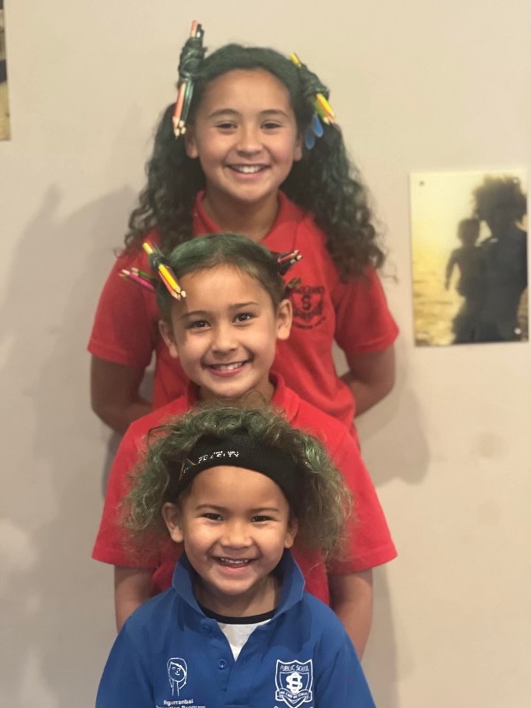 Three children in school uniform smile for the camera.