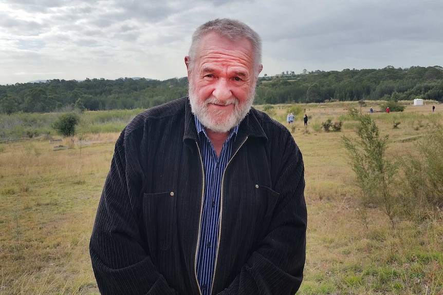 A man stands in a field surrounded by remnants of buildings.