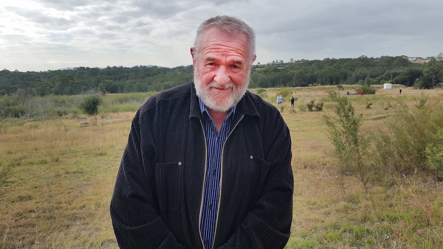 A man stands in a field surrounded by remnants of buildings.