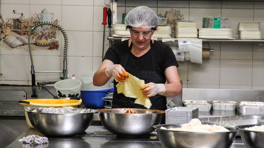 A woman wearing safety gear hand makes pasta pockets.