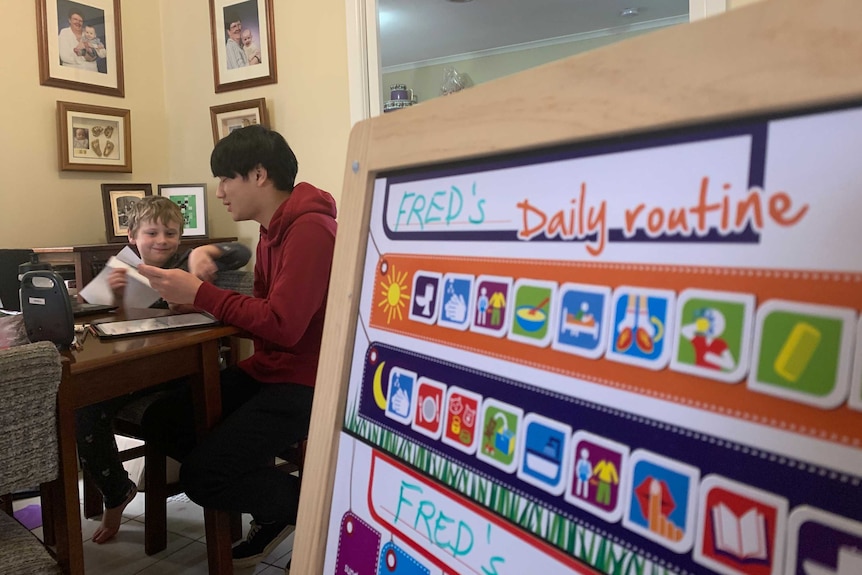 Frederick Haynes works with his support worker in the background, his daily routine is on a board in the foreground.