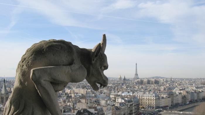 A view of buildings in Paris behind a gargoyle on the roof of Notre Dame cathedral
