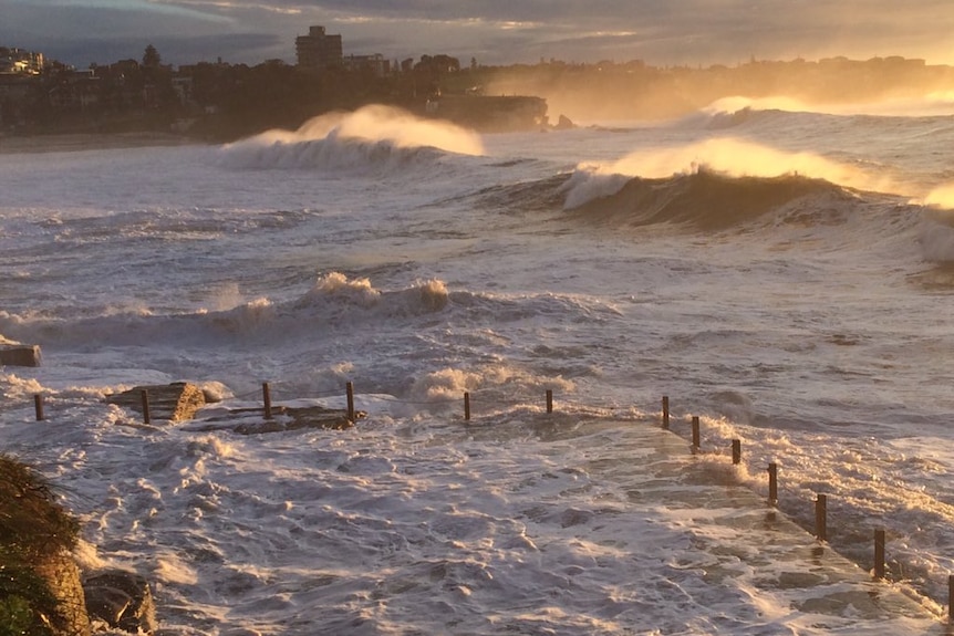 A view of an ocean pool and Coogee Bay with huge waves, white, foamy water.