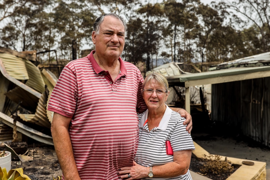a man and his wife standing outside their burnt down home