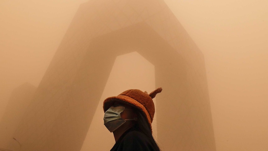 A woman stands in front of a modern building covered in smog in Beijing