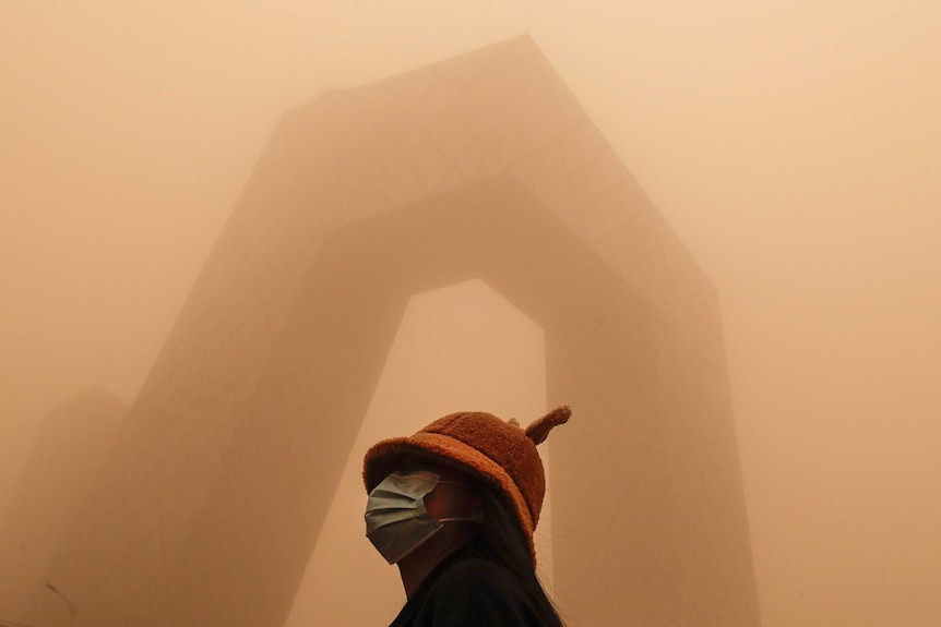 A woman stands in front of a modern building covered in smog in Beijing