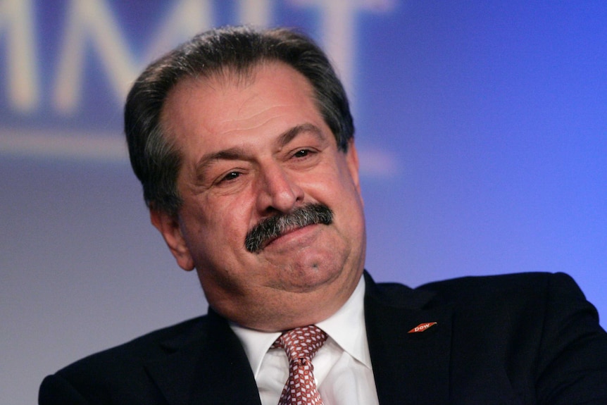A man with a moustache wearing a suit with a red tie.