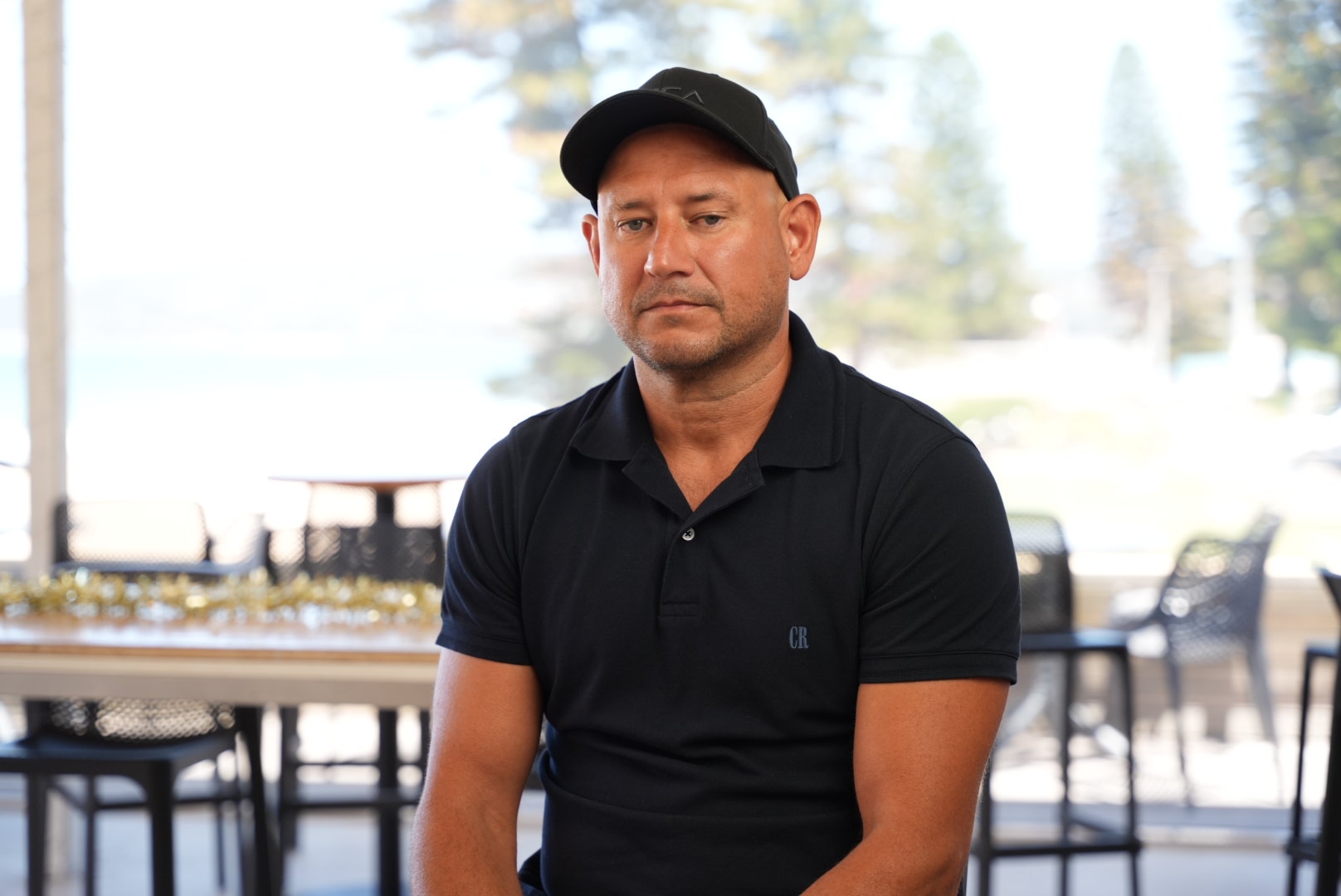 Un primer plano de un hombre vestido con una camiseta negra y una gorra.
