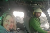 A selfie of a man and a woman wearing helmets and headsets inside a helicopter, the man is driving.