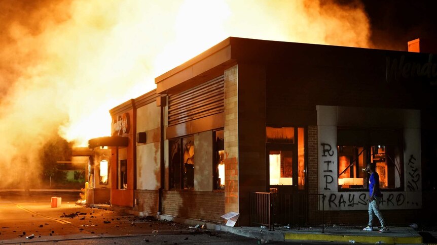 a wendy's fast food restaurant burning with a person standing nearby