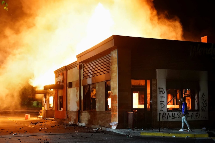 a wendy's fast food restaurant burning with a person standing nearby