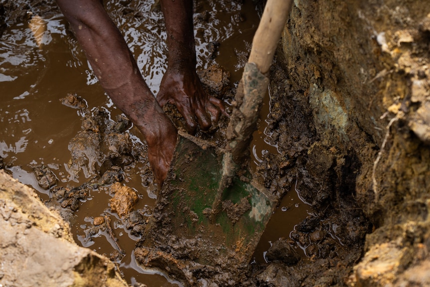 A shovel covered in mud being used to dig
