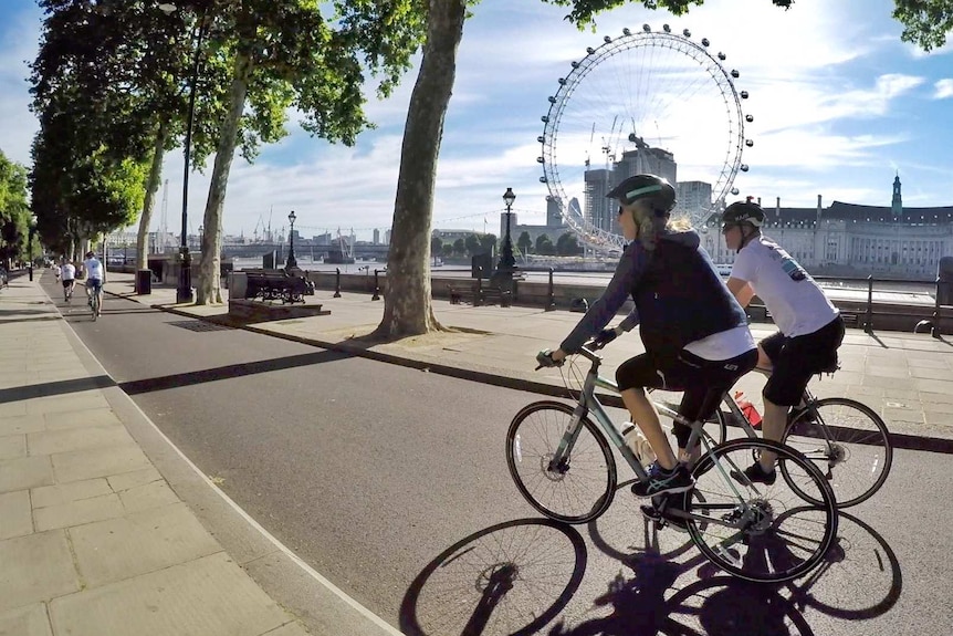People cycling along a path with the London Eye in the background.