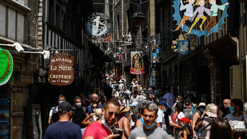 A crowded and narrow street with some people wearing face masks