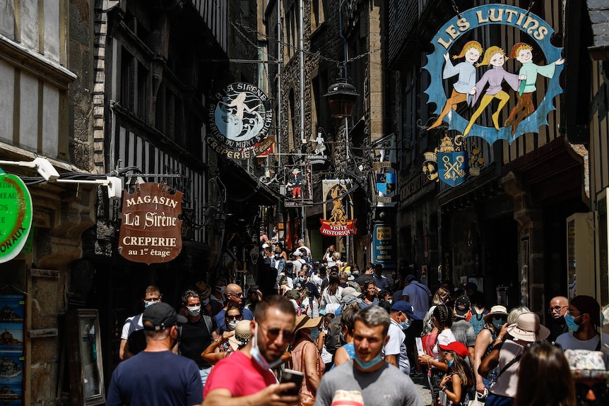 A crowded and narrow street with some people wearing face masks