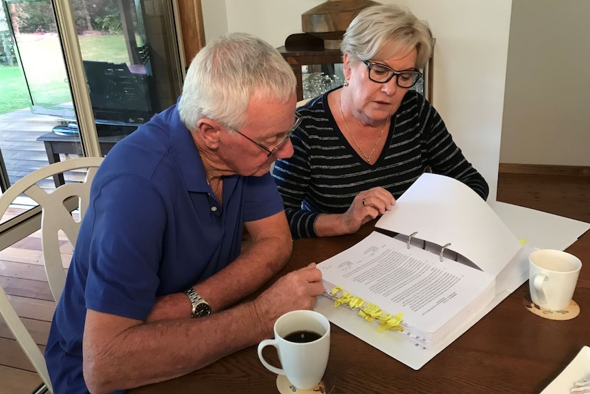 A mature couple sit at a table looking through a folder of paperwork