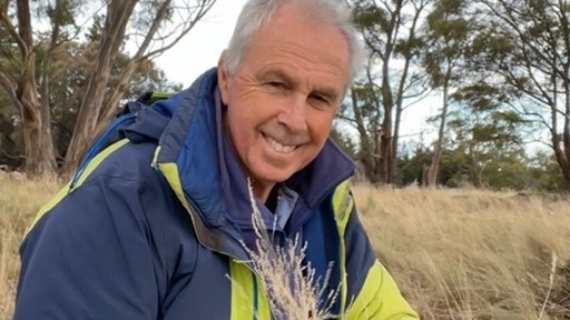 A white haired man looking at the camera and holding some grass on an east coast property in Tasmania