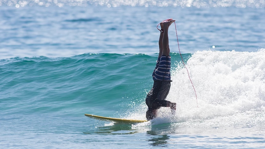 Surfer does a headstand while riding a wave at Crescent Head, NSW.