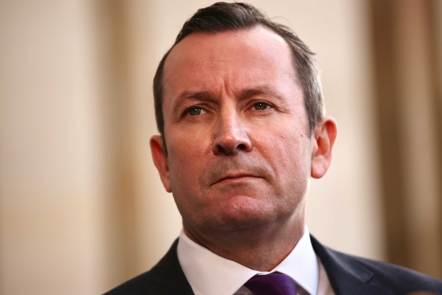 WA Premier Mark McGowan standing outside parliament looks serious wearing a suit and purple tie.