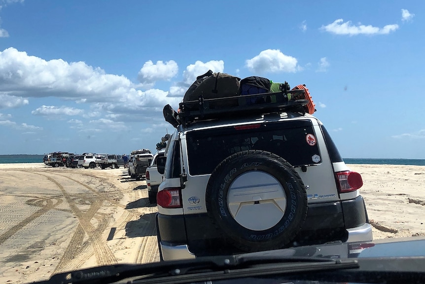 A queue of 4WDs on a beach