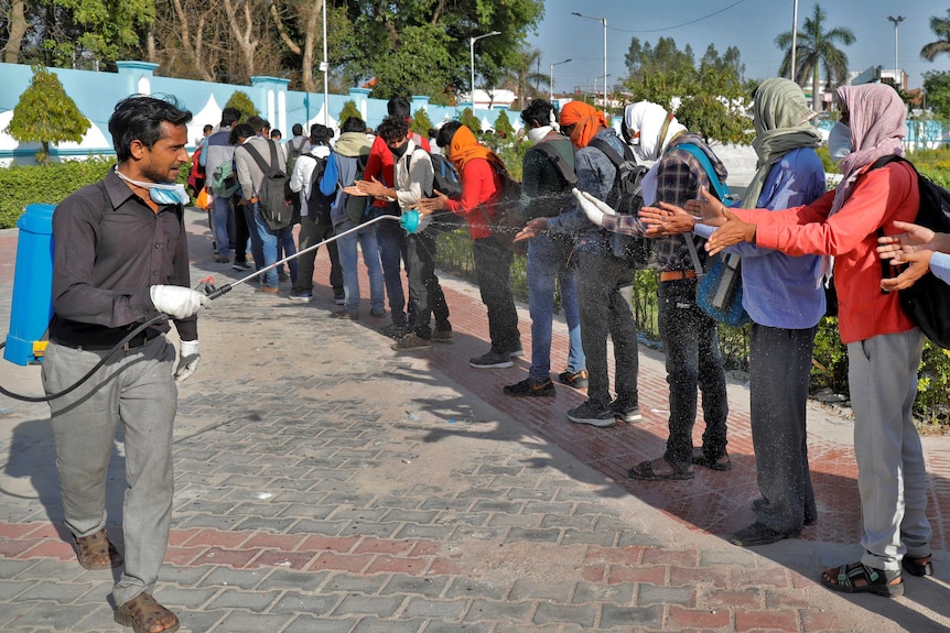 A man sprays disinfectant from a hose onto people's hands as they line up.