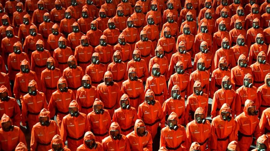 Personnel in orange hazmat suits march during a paramilitary parade.