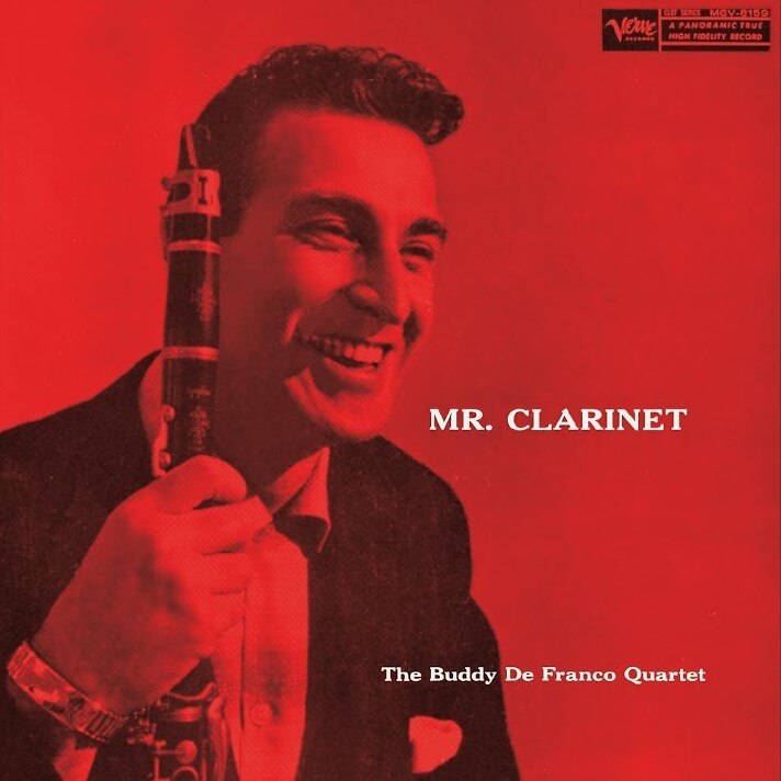 A red-hued photo of Buddy DeFranco with his clarinet, looking to the right of the frame and smiling