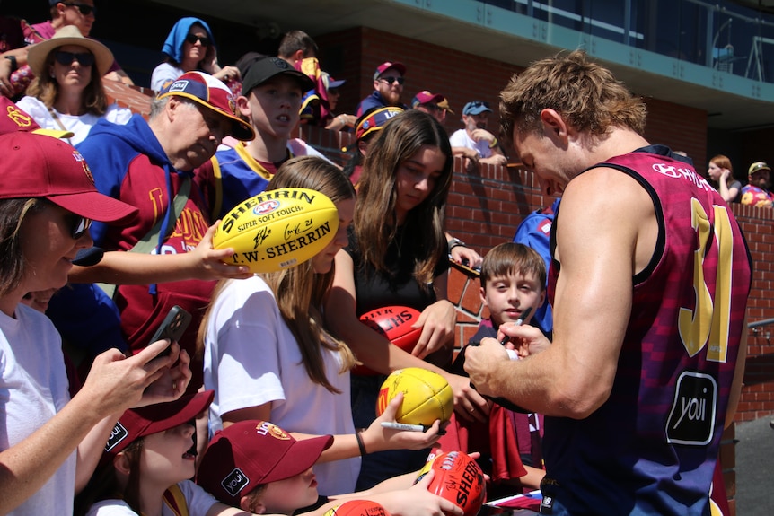 Fans gather around a Brisbane Lions player, awaiting autographs