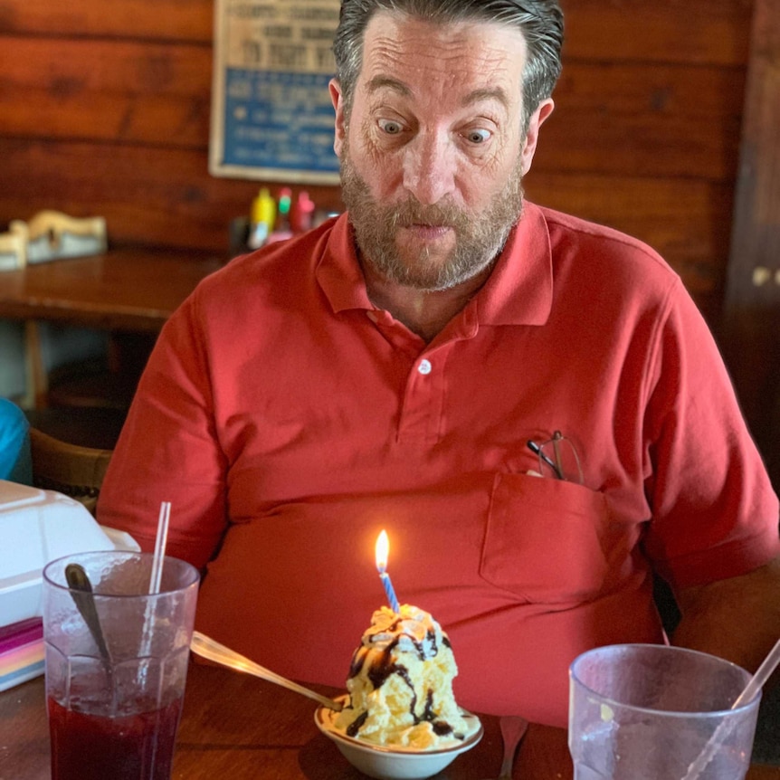 A man looks down at a bowl of ice cream with a candle in it