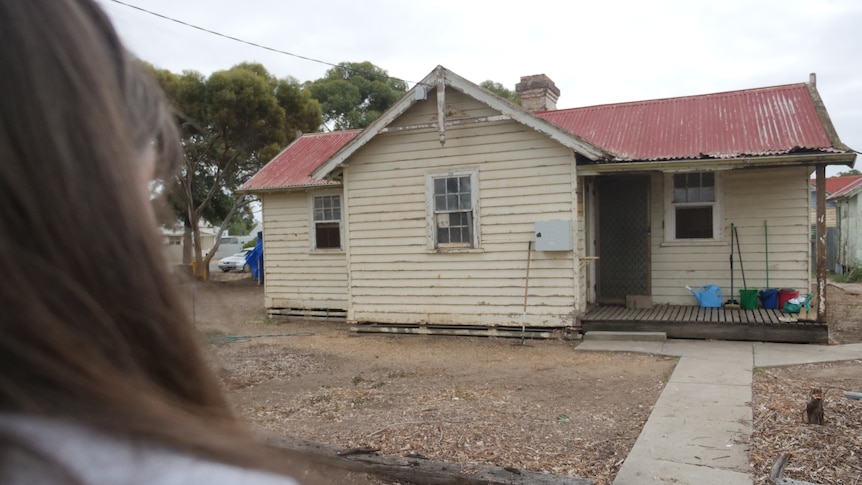 out of focus women's hair looking at a red roof, beige weatherboard home with empty yard