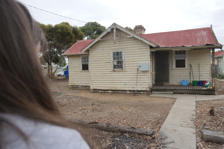 out of focus women's hair looking at a red roof, beige weatherboard home with empty yard