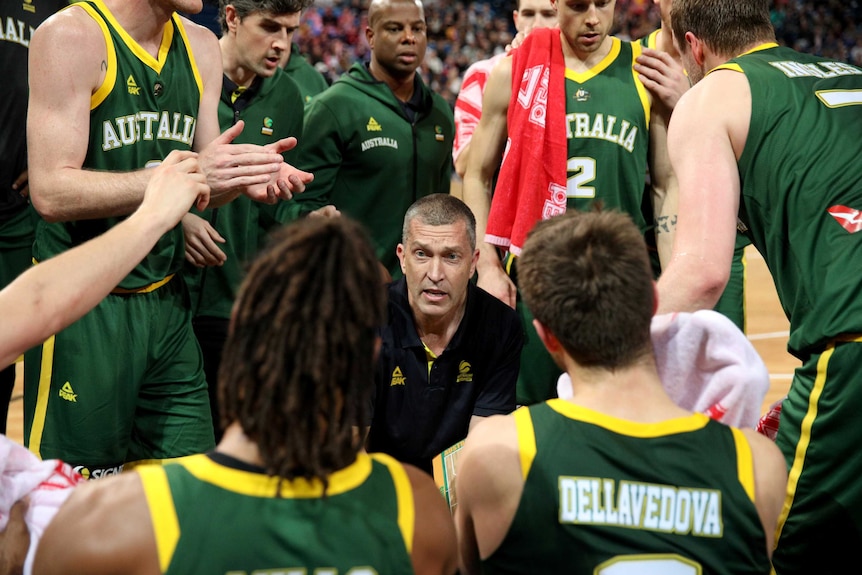 A basketball coach on his haunches gives a team talk to a circle of his players during a match.