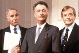 The three main characters from British political satire Yes Minister stand together wearing suits.