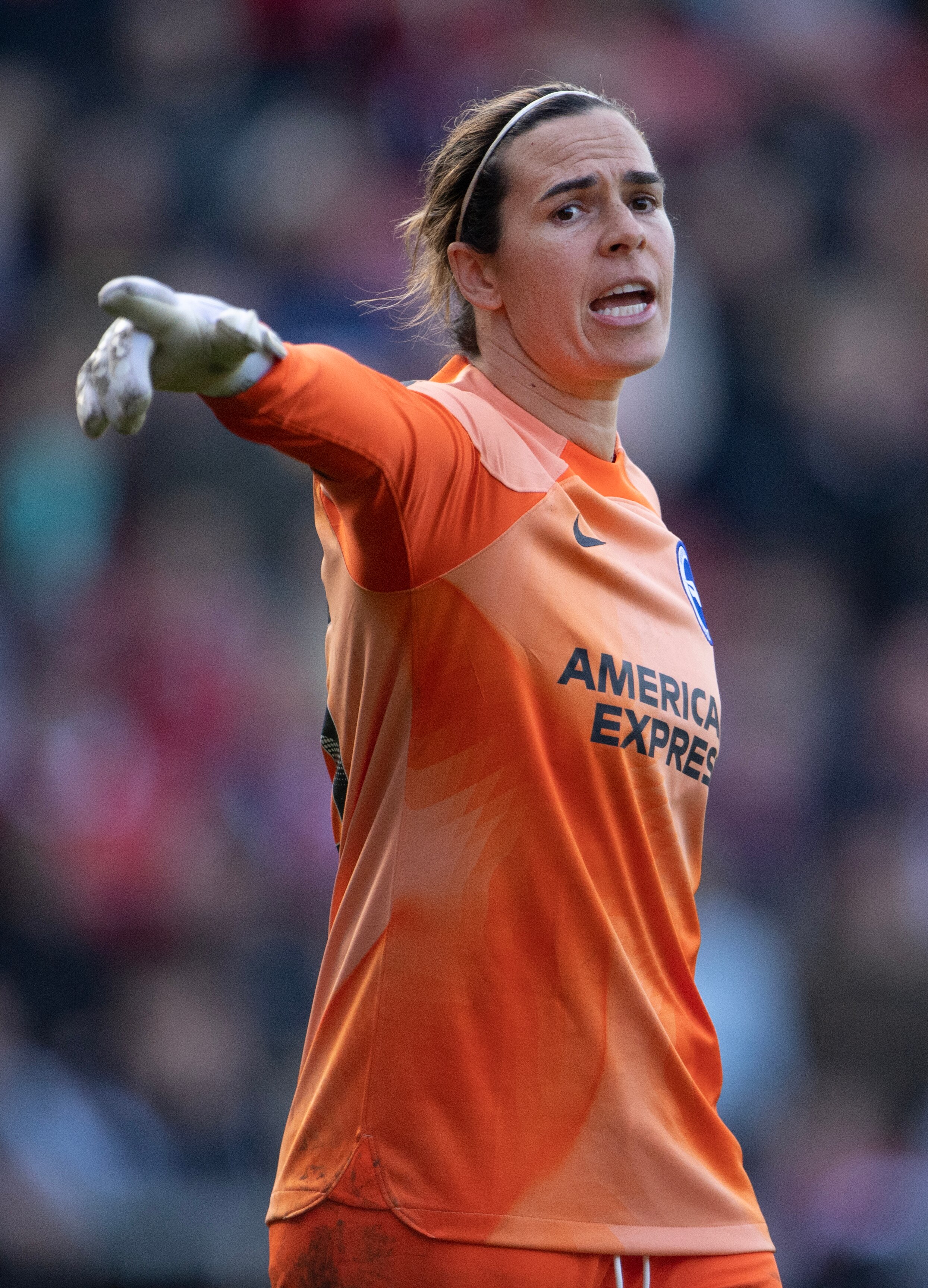 Australia goalkeeper Lydia Williams playing for English team Brighton. She is pointing and she is wearing an orange jersey.