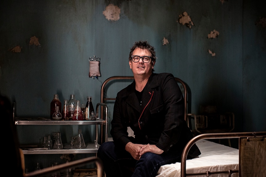 Colour photo of A Midnight Visit creative producer Simon Hayward sitting in a 19th century degraded hospital ward theatre set.