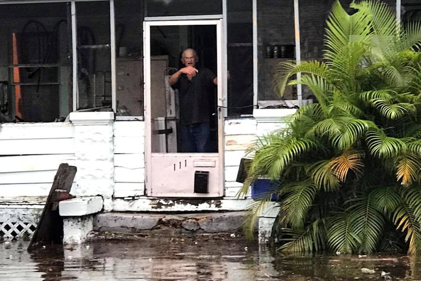 A man gestures to police officers from a flooded house.