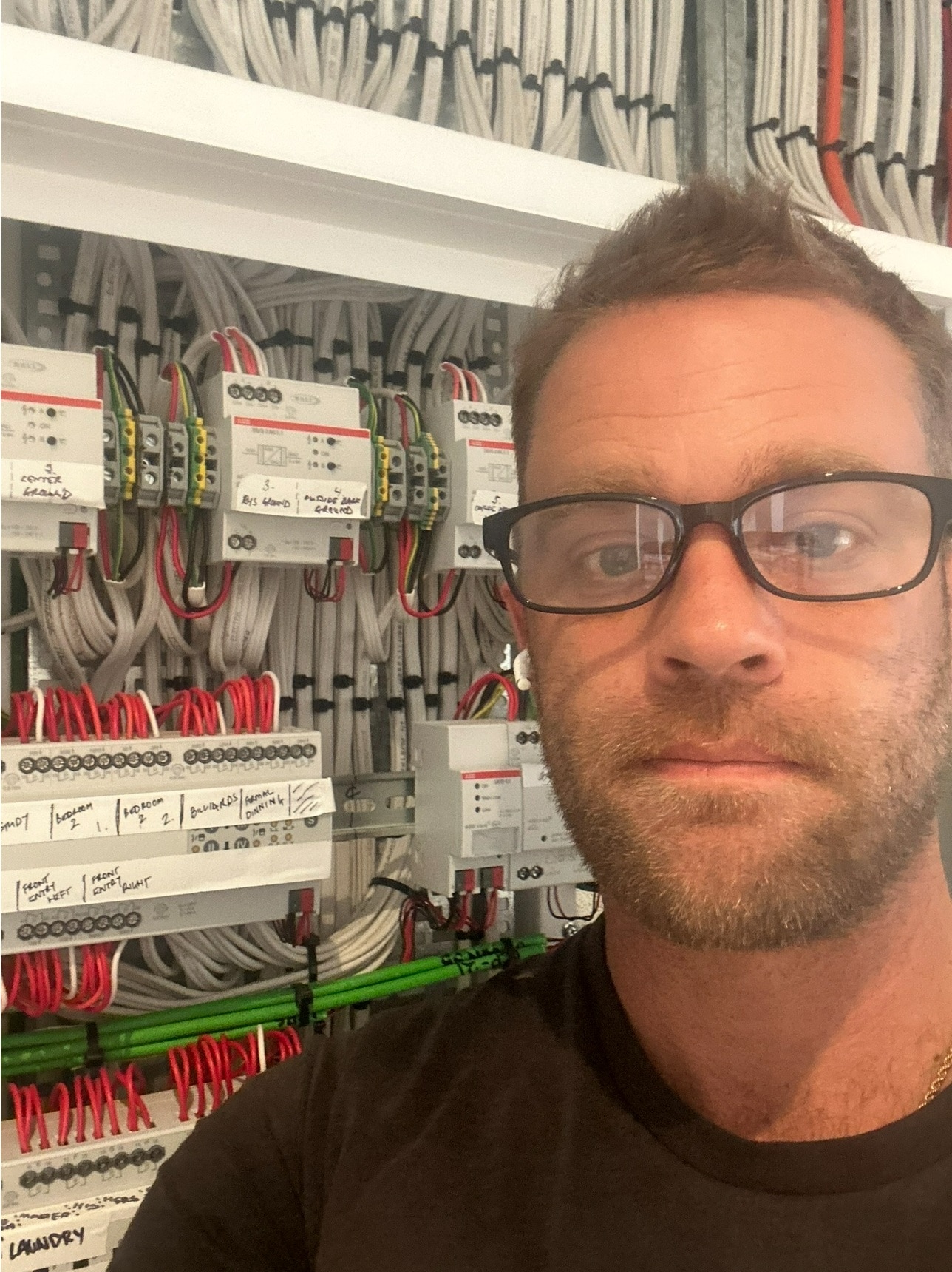 A man in his early 40s wearing reading glasses, blonde hair, standing in front of electrical supplies