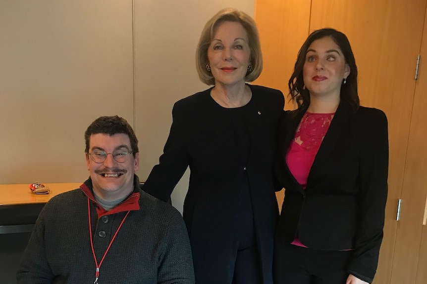 A man and two women are standing together, looking at the camera and smiling.