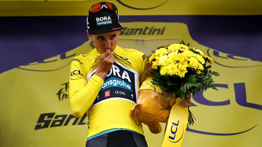 Jai Hindley kisses the yellow jersey on a podium at the Tour de France.