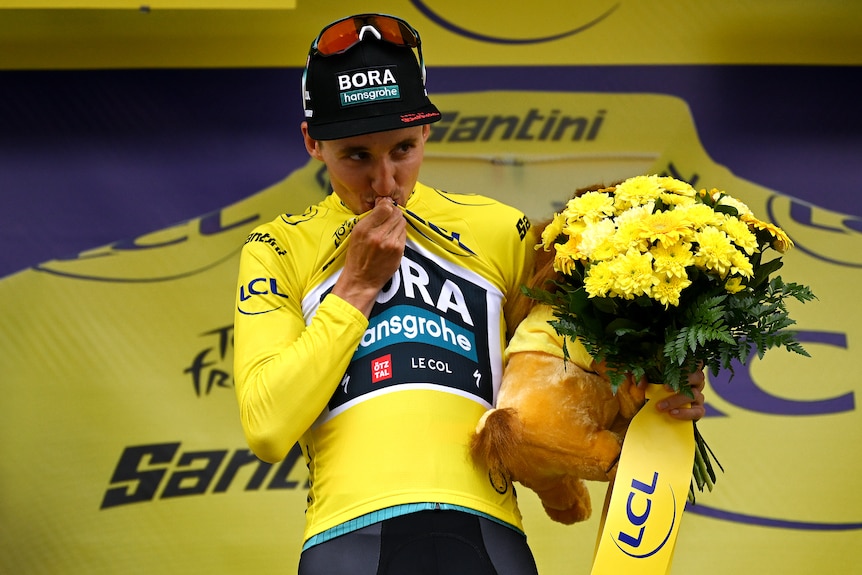 Jai Hindley kisses the yellow jersey on a podium at the Tour de France.