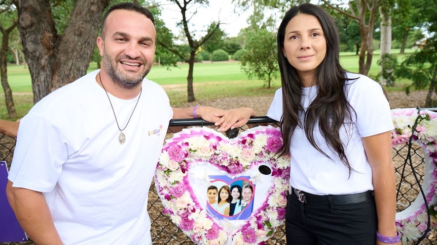 Daniel and Leila Abdallah stand either side of a paper and flower heart-shaped artwork with their children's photos.