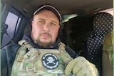A man with a beard wear military camouflages sitting in a car. 