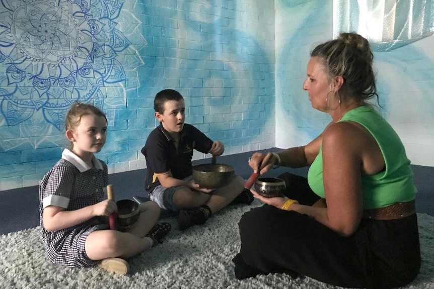 Two students sit on the floor of the school's meditation room with a teacher.