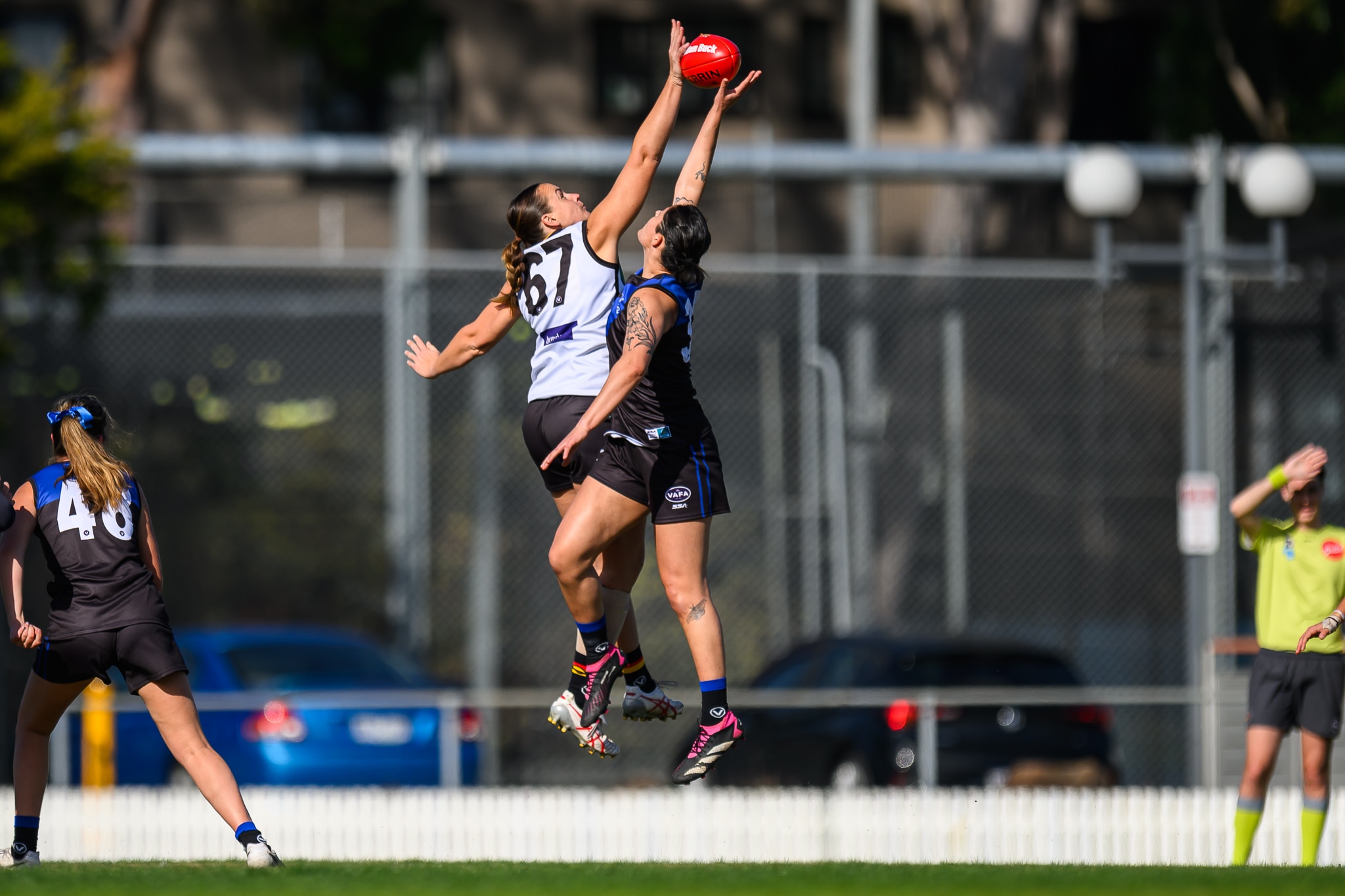 Duas mulheres estão no ar, depois de pular e pegar uma bola de futebol em uma partida de futebol australiano. 