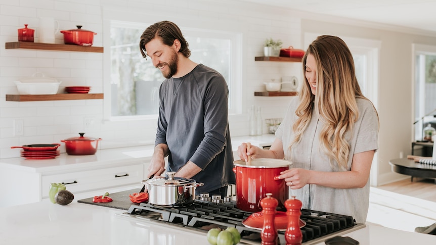 A couple cooking side by side on a gas stove.